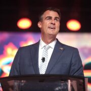 Kevin Stitt stands in front of a microphone.