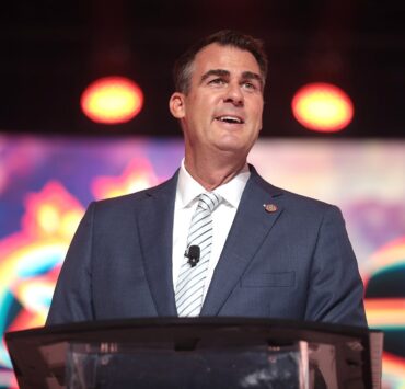Kevin Stitt stands in front of a microphone.