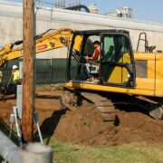 A man sits in an excavator and moves dirt in a cemetery