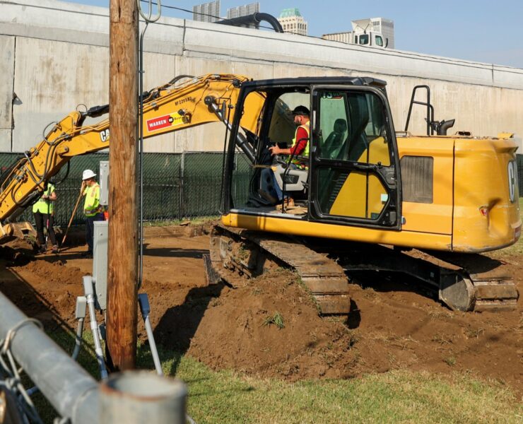 A man sits in an excavator and moves dirt in a cemetery
